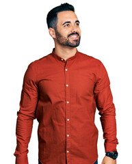 Young hispanic man with beard wearing casual shirt looking away to side with smile on face, natural expression. laughing confident.