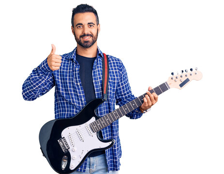 Young hispanic man playing electric guitar smiling happy and positive, thumb up doing excellent and approval sign