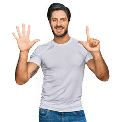 Young hispanic man wearing casual white t shirt showing and pointing up with fingers number seven...