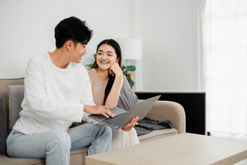 Young couple enjoys a personal moment while working on a laptop in a clean, minimalist living room with natural light.