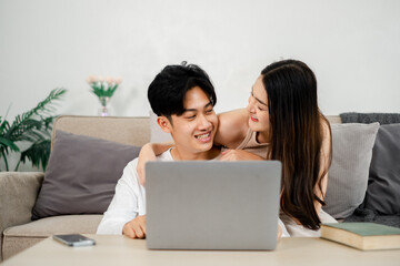 Young couple shares a laugh over something amusing on their laptop in a comfortable home setting.