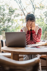 Young woman feeling overwhelmed and stressed while working from home, with hands covering her face in front of a laptop.