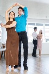Enthusiastic young couple, elegant guy and attractive girl in formal wear, performing kizomba in studio class setting, demonstrating dance characteristic sensual and connected movements..