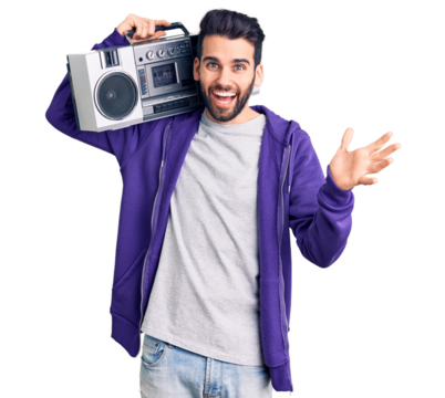 Young handsome man with beard listening to music using vintage boombox celebrating victory with happy smile and winner expression with raised hands - Powered by Adobe