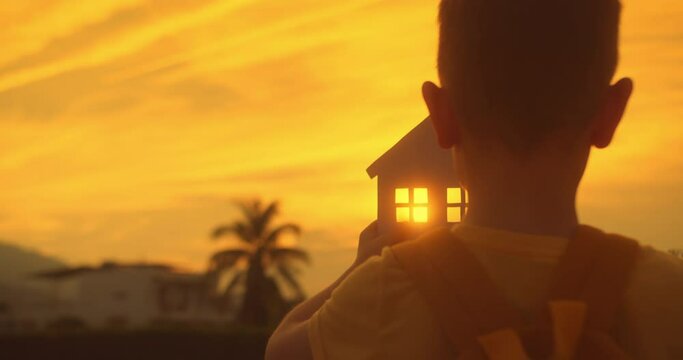 Concept of Happy Family Purchase Property, Home, Life, Insurance, Care, Savings, Mortgage, Estate. Symbol happiness. Child little girl male hands holding model of a paper house on sunset background