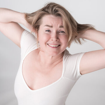 Portrait of mature adult woman with hands behind head and toothy smile. Happy woman is wearing bodysuit. High angle shot perfectly captures blonde woman's infectious energy and positive attitude