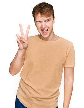 Young caucasian man wearing casual clothes smiling with happy face winking at the camera doing victory sign with fingers. number two.