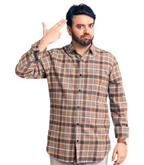 Naklejka premium Young hispanic man wearing casual clothes shooting and killing oneself pointing hand and fingers to head like gun, suicide gesture.