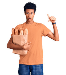Young african american man holding paper bag with bread pointing down with fingers showing...