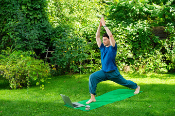 a man does yoga in nature online using a laptop - 780968113