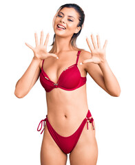 Young beautiful woman wearing bikini showing and pointing up with fingers number ten while smiling...