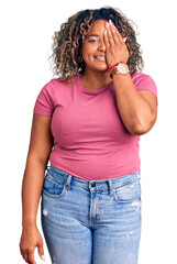 Young african american plus size woman wearing casual clothes covering one eye with hand, confident smile on face and surprise emotion.