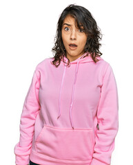 Young hispanic woman wearing casual sweatshirt in shock face, looking skeptical and sarcastic,...