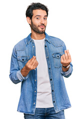 Young hispanic man wearing casual clothes doing money gesture with hands, asking for salary...
