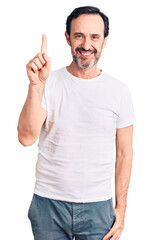 Fototapeta premium Middle age handsome man wearing casual t-shirt showing and pointing up with finger number one while smiling confident and happy.