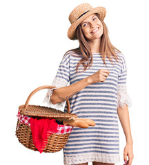 Beautiful caucasian woman wearing summer hat and holding picnic wicker basket with bread looking positive and happy standing and smiling with a confident smile showing teeth