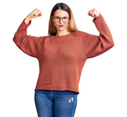 Beautiful young woman wearing casual clothes and glasses showing arms muscles smiling proud. fitness concept.
