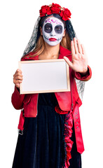 Woman wearing day of the dead costume holding empty white chalkboard with open hand doing stop sign with serious and confident expression, defense gesture
