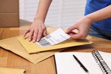 Parcel packing. Post office worker sticking barcode on bag at wooden table indoors, closeup