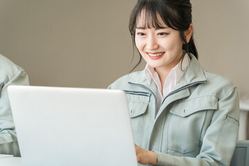 パソコンで仕事する作業服・作業着姿の若いアジア人ビジネスウーマン（建築士・設計士）
