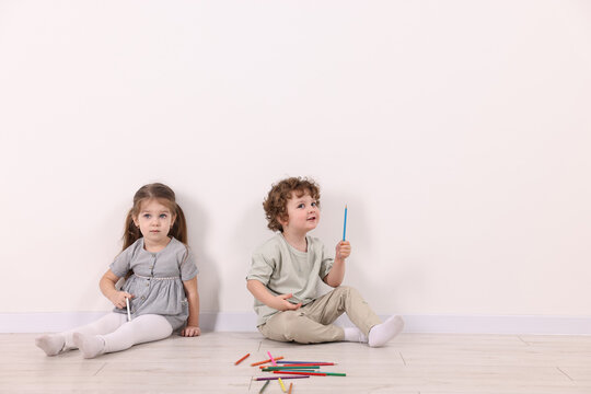 Cute little children with colorful pencils near white wall indoors. Space for text