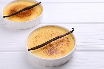 Delicious creme brulee in bowls and vanilla pods on white wooden table