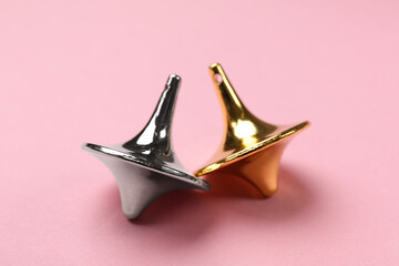 Golden and silver spinning tops on pink background, closeup