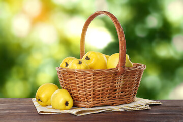 Fresh ripe quinces in wicker basket on wooden table outdoors