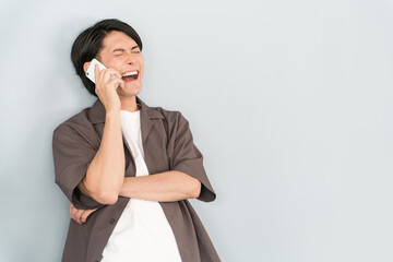スマホで通話・電話する若いアジア人男性（爆笑・談笑・笑う）
