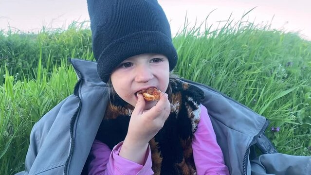 Hungry little girl eats bread Homeless child Little refugee in hat with earflaps having food to eat on the land