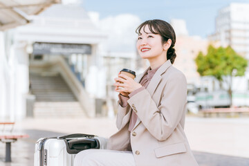 出張・旅行でバス停・タクシー乗り場・待合所でコーヒー・紅茶を飲む女性（待ち合わせ）
