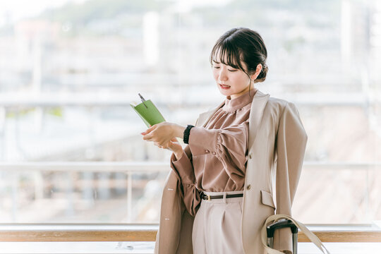 スケジュール帳を見ながら腕時計で時間を確認するビジネスウーマン・若い女性
