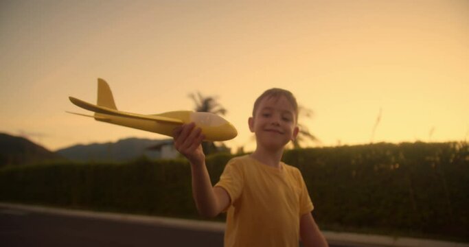 Happy kid runs with a toy airplane on park in the sunset light. Children play toy airplane. Little boy dreams of flying and becoming pilot. Child wants to become pilot and astronaut. Slow motion.