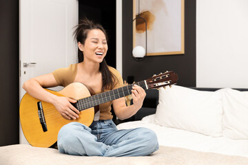 Joyful Asian Woman Playing Acoustic Guitar In Bedroom. Casual Home Entertainment, Music Hobby, Leisure Time Concept. Happy, Relaxing, Musical Instrument, Learning, Practice.