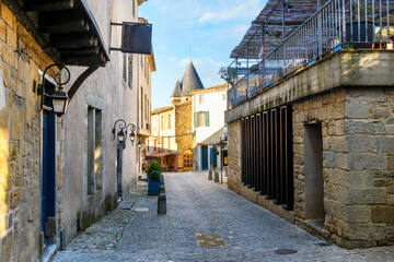 A narrow street heading towards shops and cafes with one of the historic watchtowers behind in La Cite', the medieval center of the historic castle in Carcassonne, France.