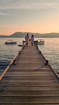 A couple strolls along the tranquil wooden dock, gazing at the calm ocean under the morning sky, with the horizon stretching across the peaceful landscape of Thailand