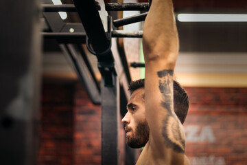 side view of a strong man doing pull ups in a gym. close-up