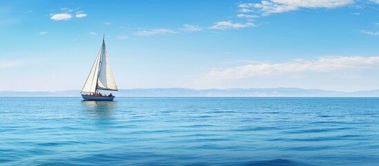 Obraz premium Sailboat peacefully sails on open sea with majestic mountains in the distance