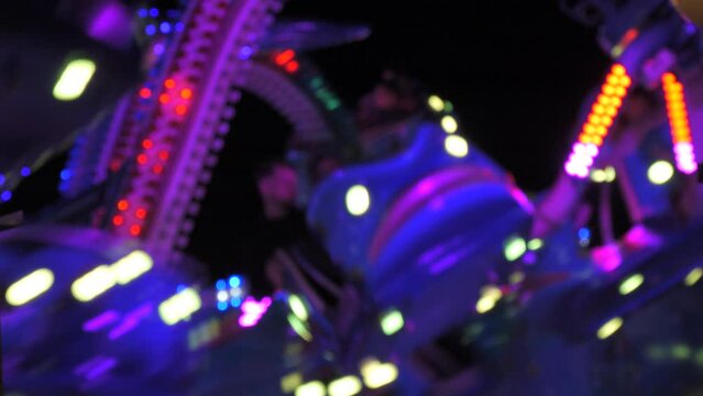 Blurred large attraction in city park of octopus head with colorful tentacles. Amusement park for family and friends. Parts of spinning attraction at entertainment site at night