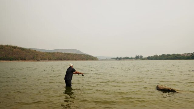 A man is standing in the water with a camera. The water is green and the sky is cloudy