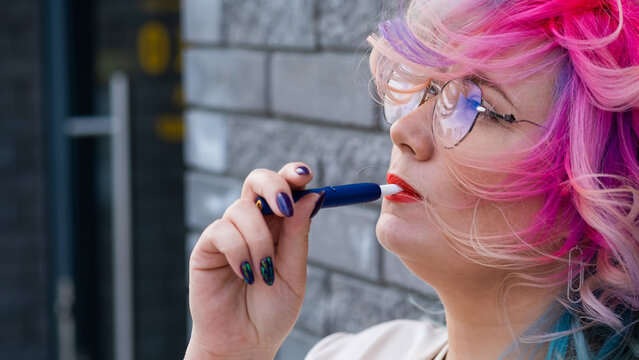 Caucasian woman with colored hair smokes an electronic cigarette.