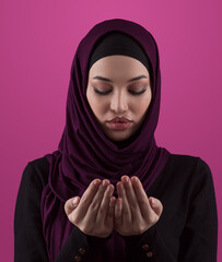 Muslim woman in hijab and traditional clothes praying for Allah, copy space. Muslim woman with hijab praying indoor pink background. - 781032575