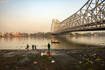 9th February, 2024, Kolkata, West Bengal, India: Beautiful landscape of a fishing boat on River Ganges crossing Howrah Bridge at the time of sunrise.