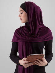 Beautiful and modern young Arabic businesswoman in hijab using a tablet computer while posing on light background and smiling at the camera. Business diversity concept, Muslim lady. - 781035377