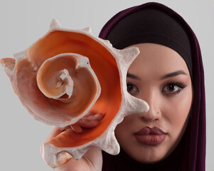 Pretty stylish Muslim woman wearing hijab and holding a seashell and dreams closed eyes. Golden...
