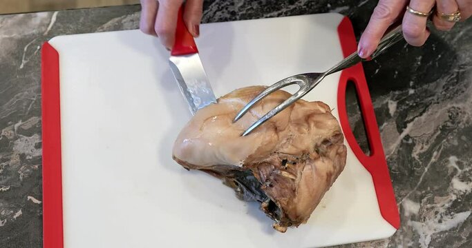 Roasted turkey breast is sliced by a person using a carving knife and a large two tined fork.