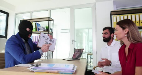 Bank manager in balaclava holds reliable banking advertisement and communicates with clients with money