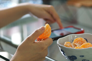 A person eats oranges while playing with a mobile phone, a Relaxing day at home concept