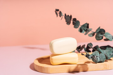 Two bars of soap in a wooden soap dish with dried flowers against a pink background.