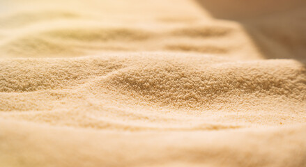 Yellow clean sand with wavy patterns under sunlight.